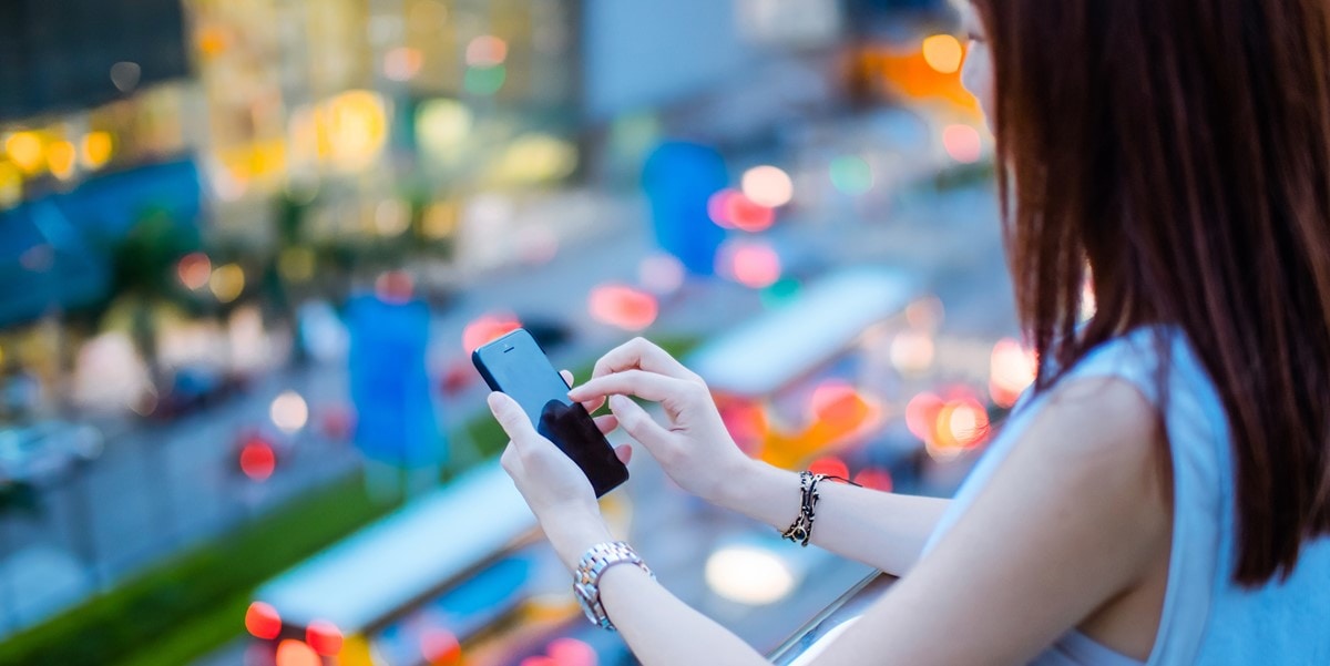 woman standing outside overlooking city, focus on phone in her hands