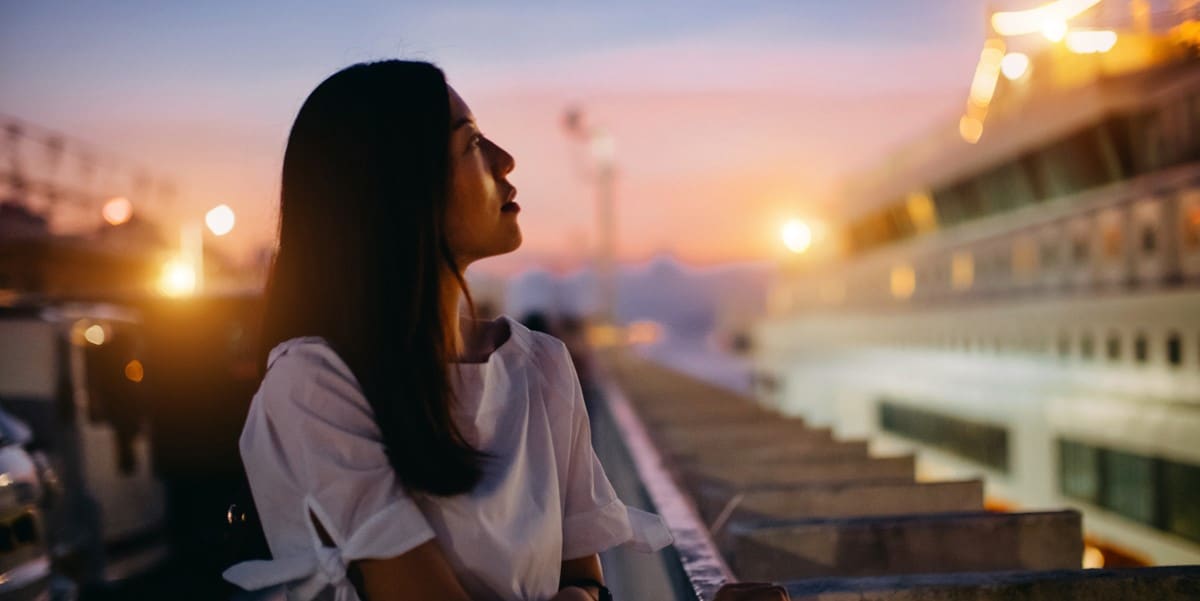 woman standing at pier at sunset looking at ferry to the right