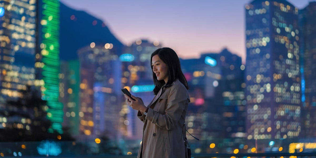 woman standing in front of cityscape, looking at phone