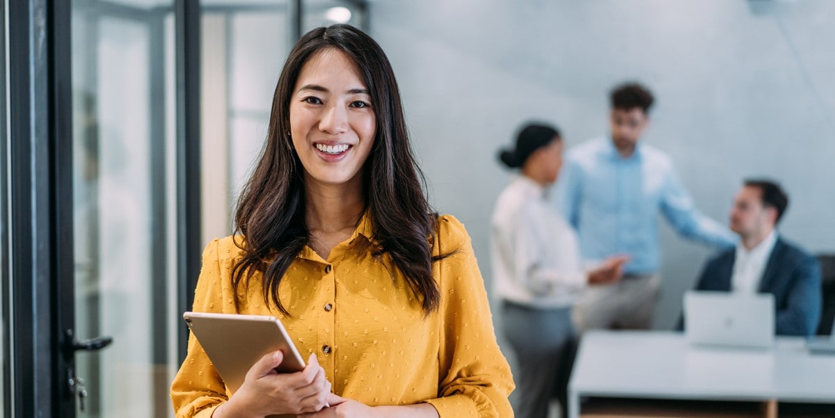 smiling woman holding tablet, in the office, group of people in the background