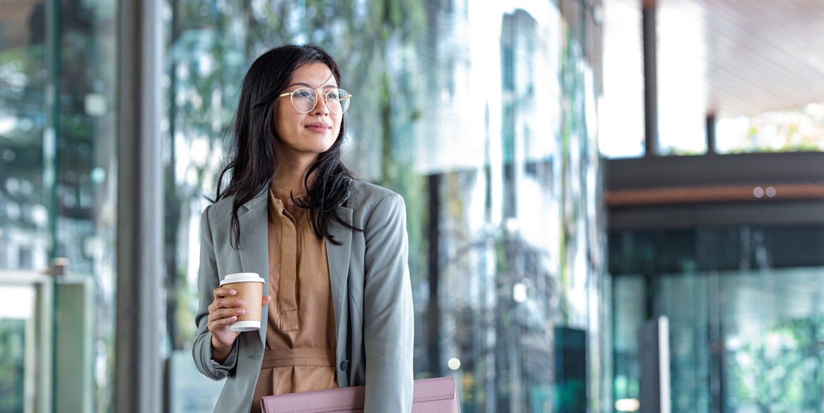 professional woman walking through office, coffee cup in hand